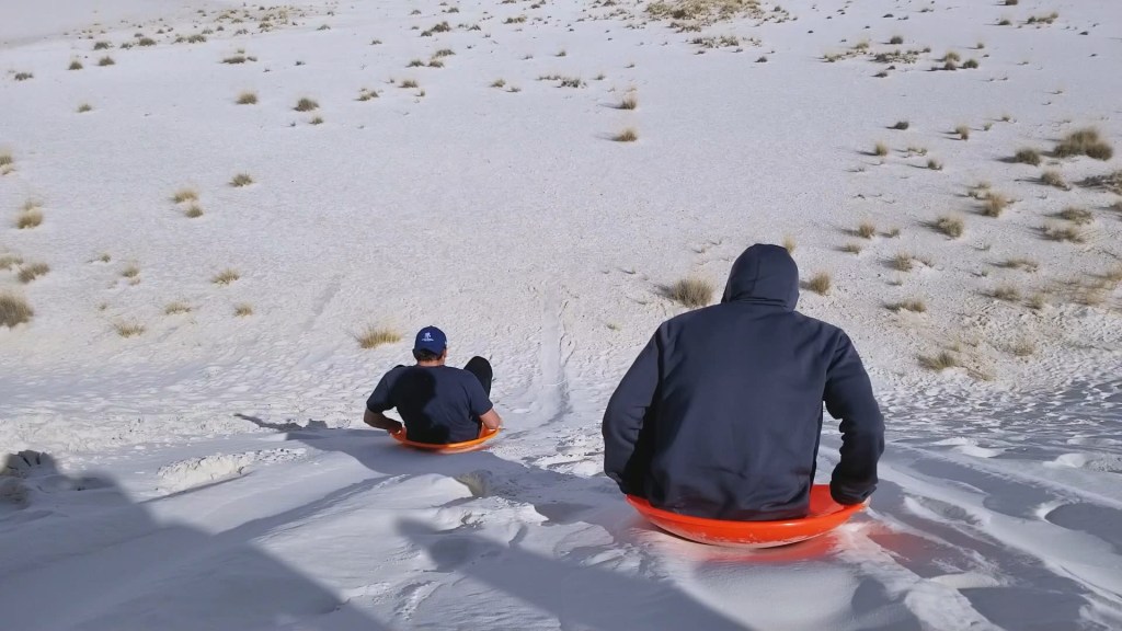 Two students sled down a dune at White Sands National Monument